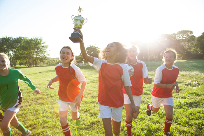 A group of five young sportspersons celebrating a win with a trophy.