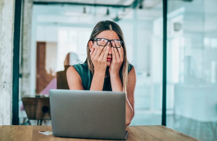 A woman rubs her eyes while sitting in front of a laptop.