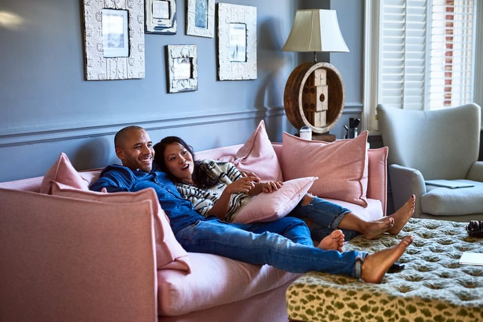 Two people lounge on a bright pink couch in a living room.