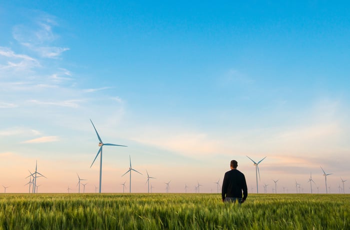 A person in a green field with wind turbines in the background.