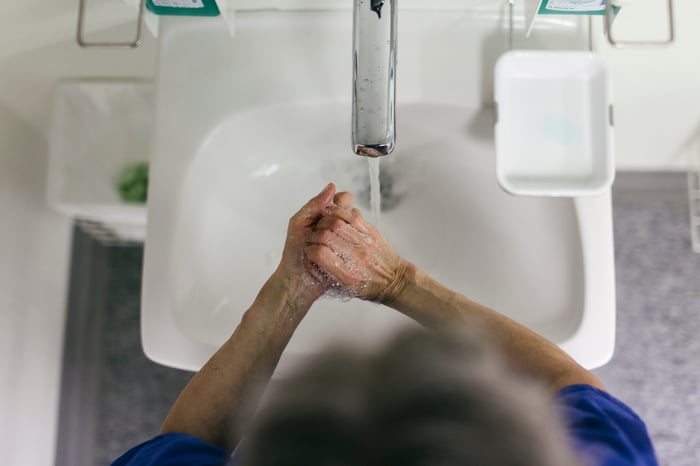 Mature adult washes their hands in a bright white sink basin.