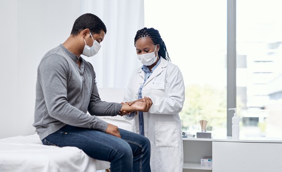 A doctor takes a patient's pulse in an examination room.