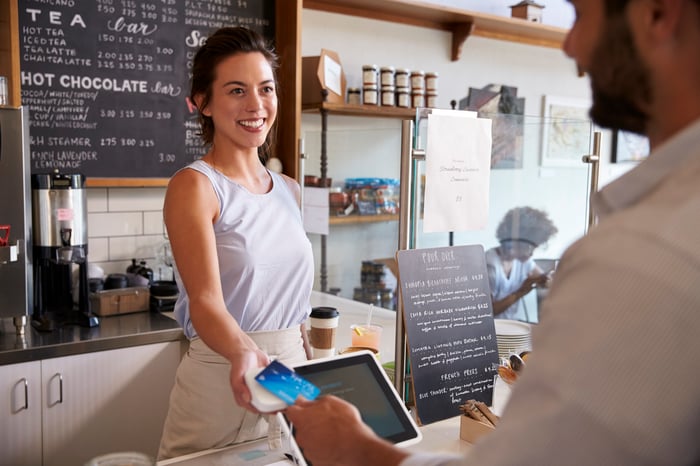 A customer paying a smiling worker for a purchase via credit card at a cafe