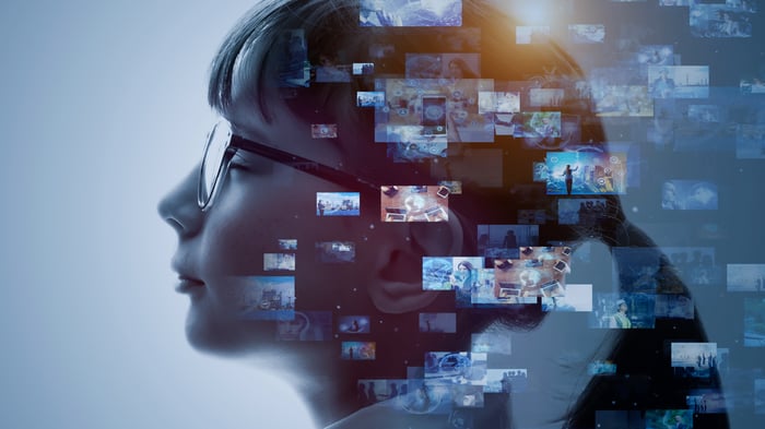 A side profile of a person's face, with glasses on surrounded by digital screens.