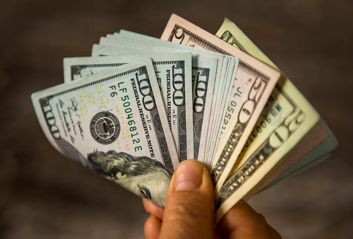 A person holding out an assortment of folded cash with their fingertips.  