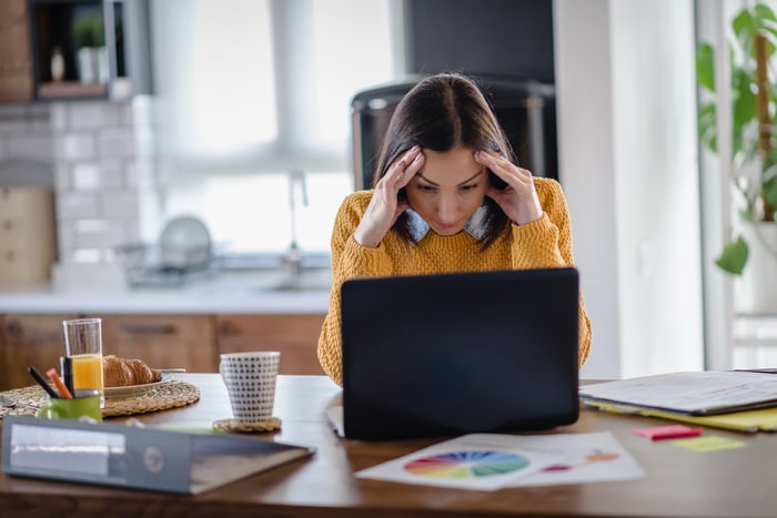 A concerned woman looks at a laptop and rubs her temples.