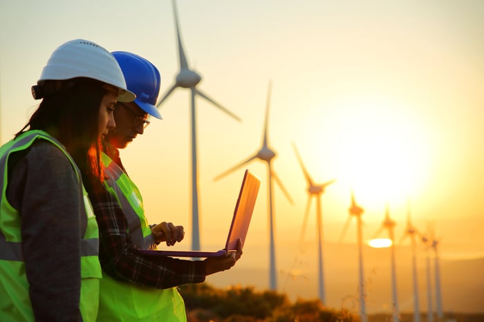 People looking at a laptop with wind turbines in the background.