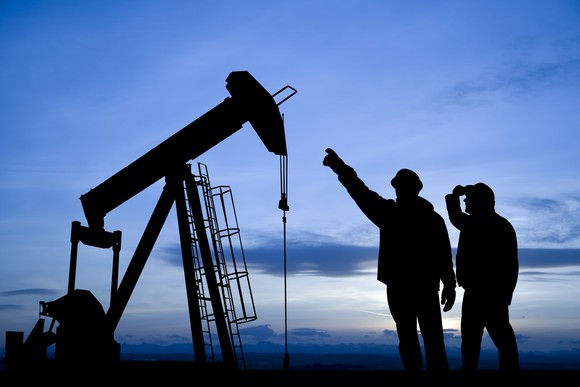 The silhouette of some people pointing to an oil well.