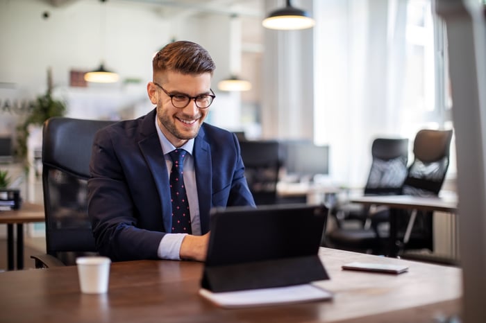 Smiling person in suit using laptop at desk.