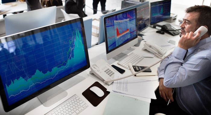 A professional broker on the phone, with multiple stock charts displayed on computer monitors. 