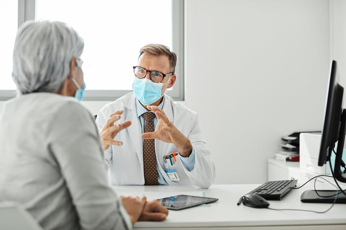 Doctor speaking to a patient and both are wearing masks.