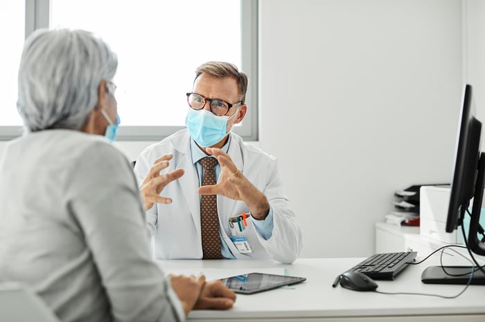 Doctor speaking to a patient and both are wearing masks. 