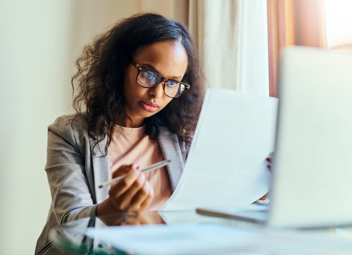 Young adult reviews documents while sitting in front of an open laptop.