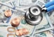 Stethoscope atop 100 dollar bills and pennies