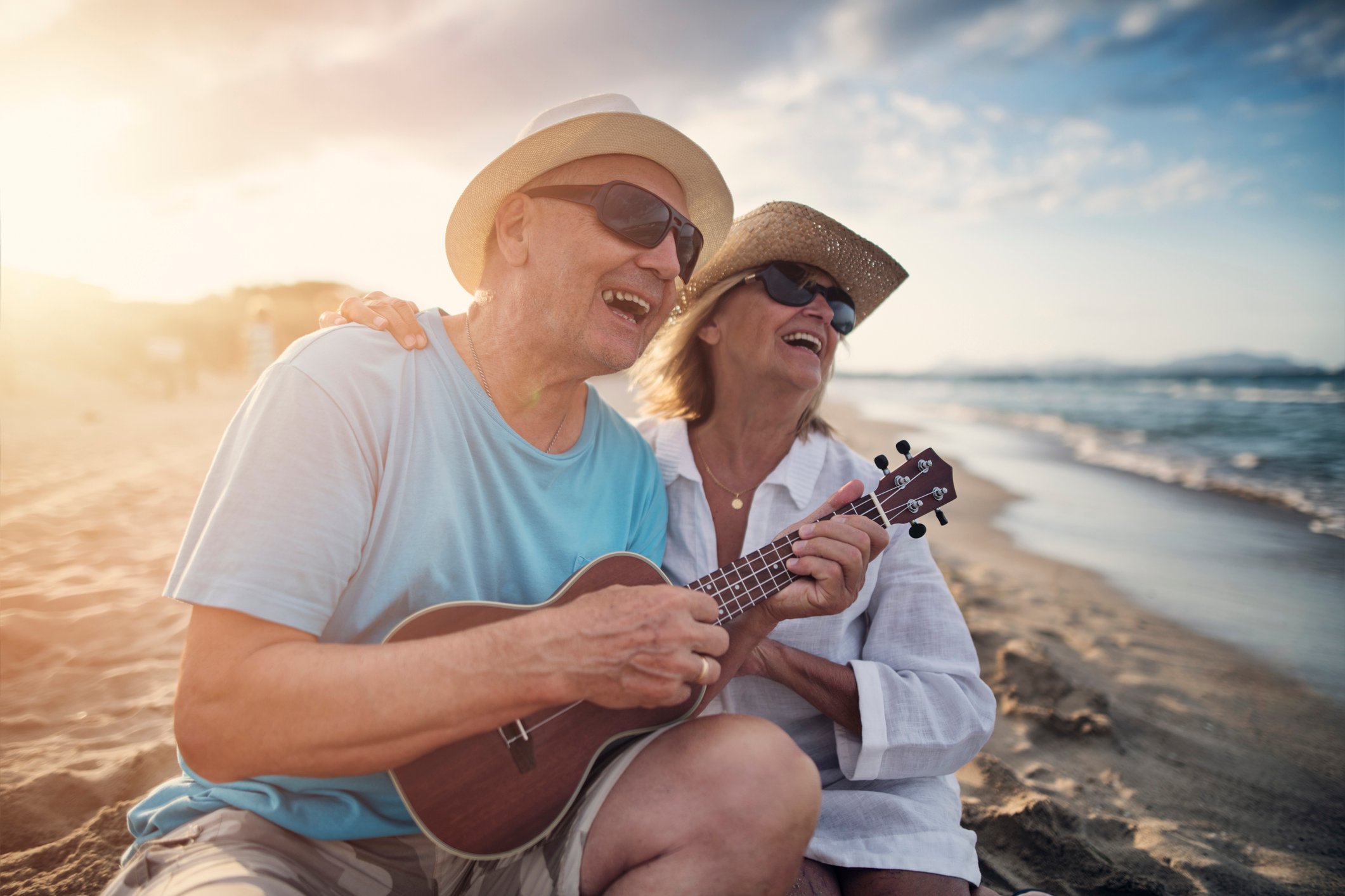 Couple sitting on beach shore smiling and playing ukelele