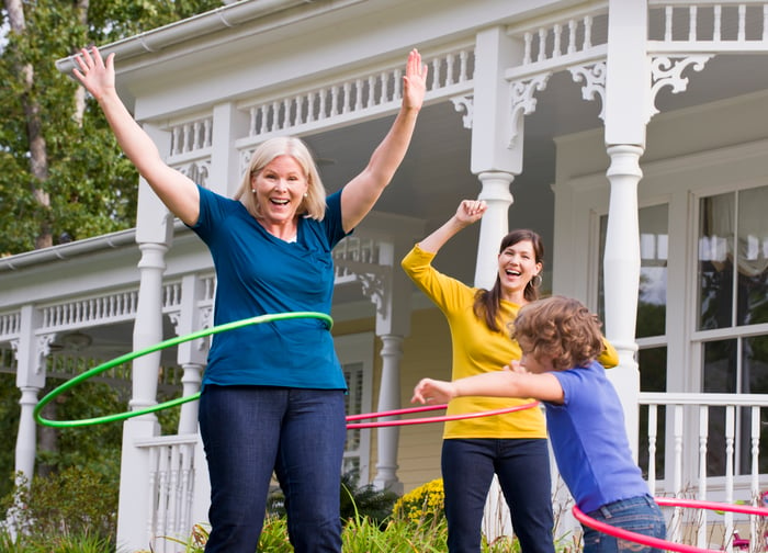 Three people from different generations hula hoop in the yard of a home. 