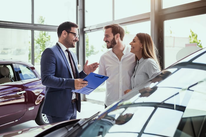 A young couple purchasing a car off a salesperson, looking extremely happy