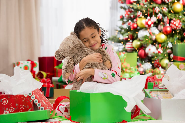 Person hugging a teddy bear with a Christmas tree in the background.