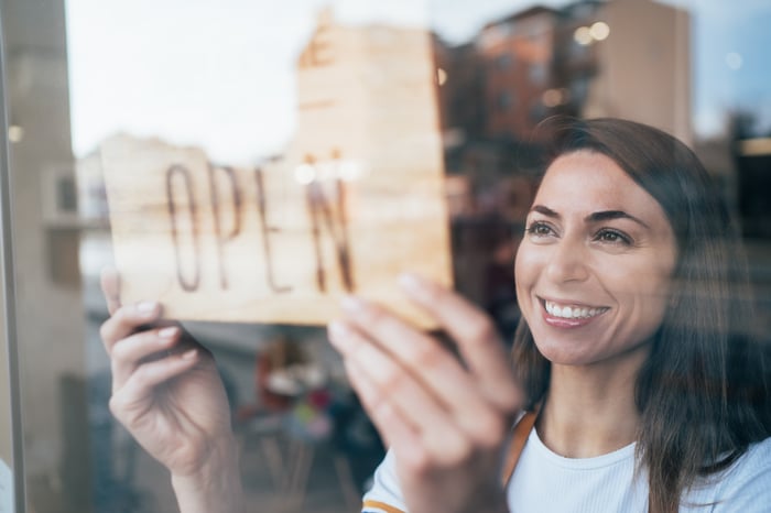 A very happy business owner hanging an open sign in their shop window