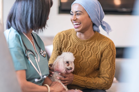 A patient holds a poodle while talking to a health worker.