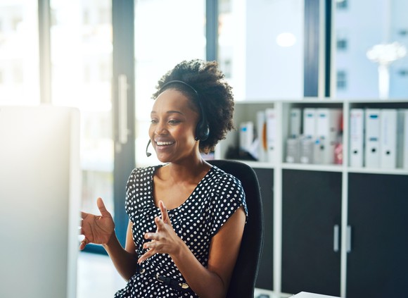 A woman wearing a headset and speaking to a customer while at her desk.