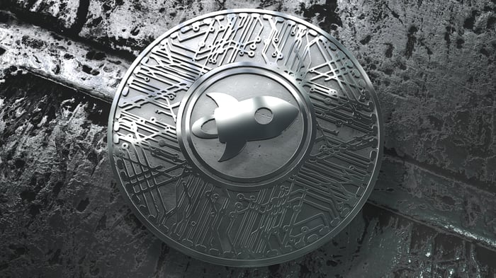 A silver Stellar Lumen coin with a rocket ship logo. 