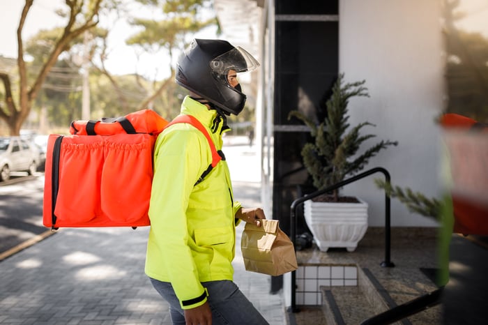 A delivery driver in a bright yellow jacket is delivering food.