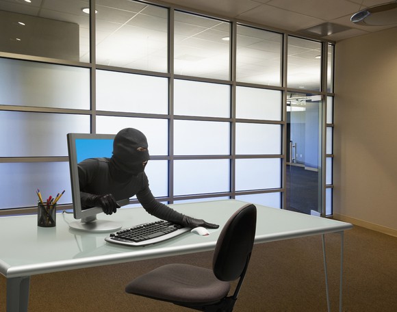 Person in black clothes and a black mask coming out of a computer screen.