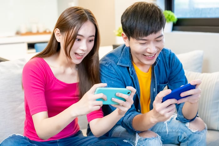 Two people sitting on a sofa look excitedly at their mobile phones.