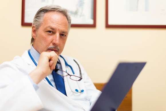A physician holding his glasses in front of his face while in deep thought.
