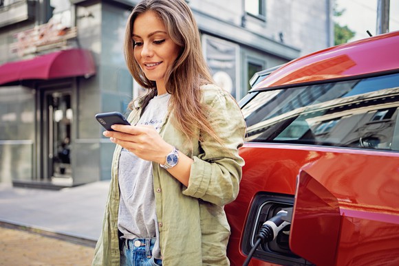 A person uses their smartphone while waiting for an electric vehicle to charge.
