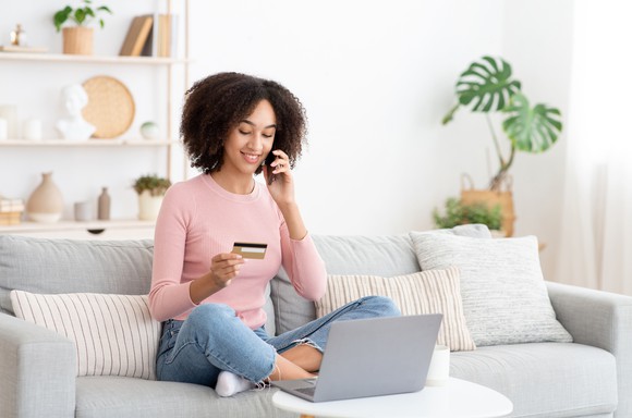 A person on their laptop and cell phone holding a credit card.