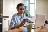 Mature person shops online while at home and holds a credit card in their hand.