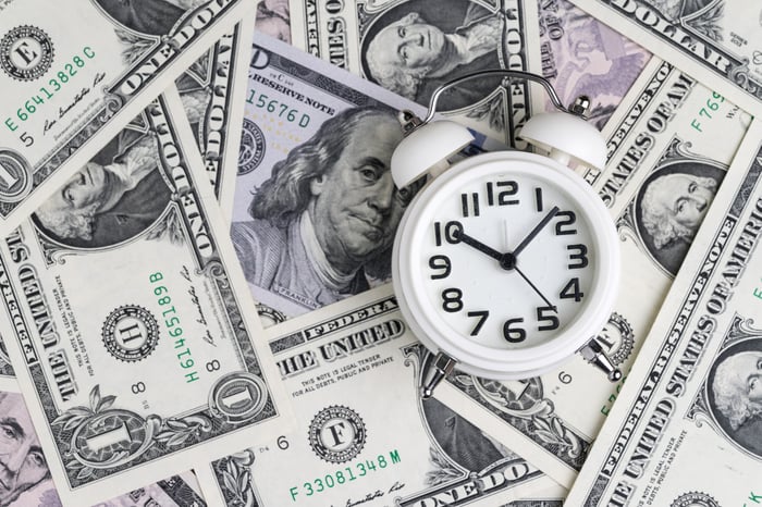 A clock is sitting atop a field of U.S. currency.