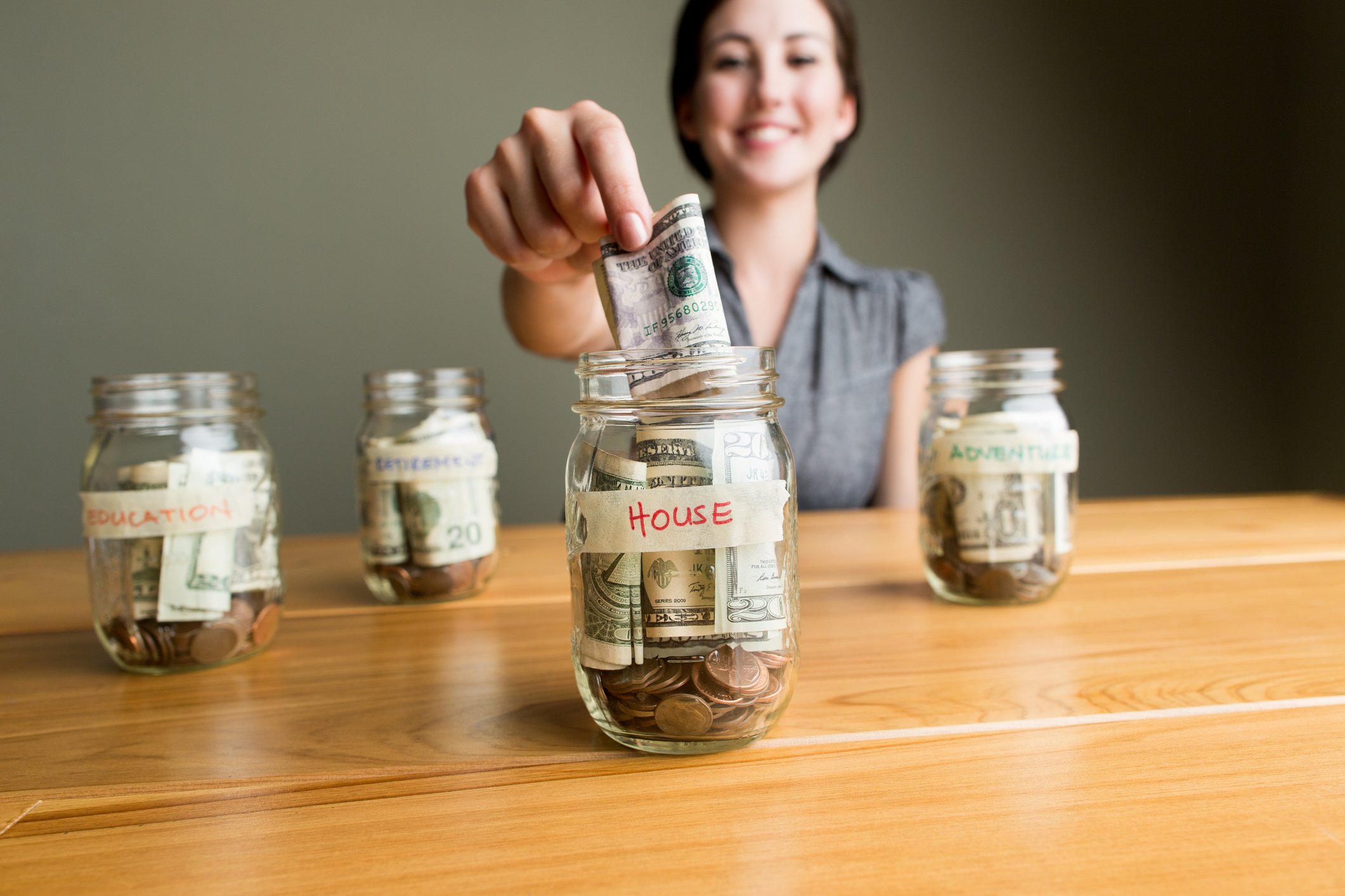 A prerson putting money into a savings jar to buy a house.