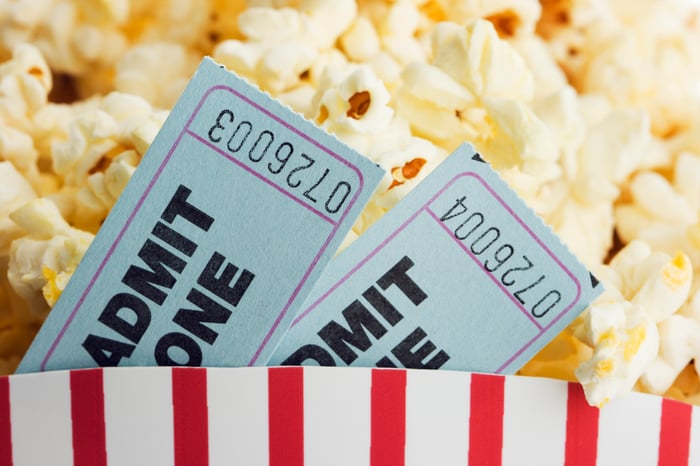 Two movie admission tickets placed in a full bucket of concession-stand popcorn.