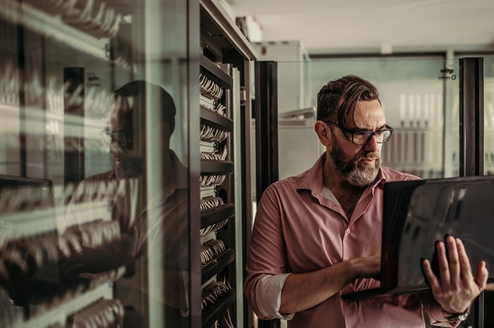 Mature adult works in a data center while holding a laptop.