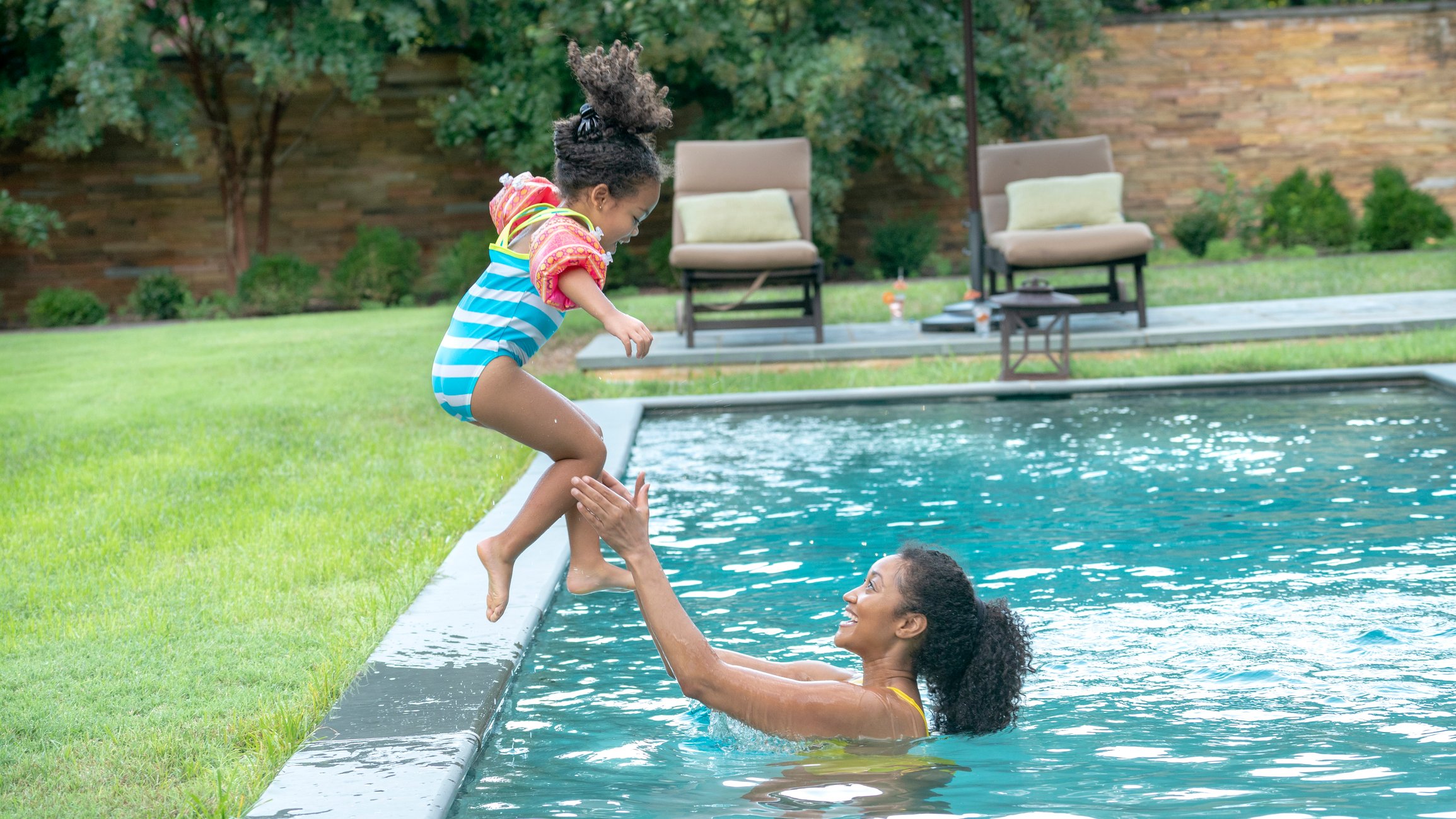 Young child jumping into a pool into the waiting arms of an adult