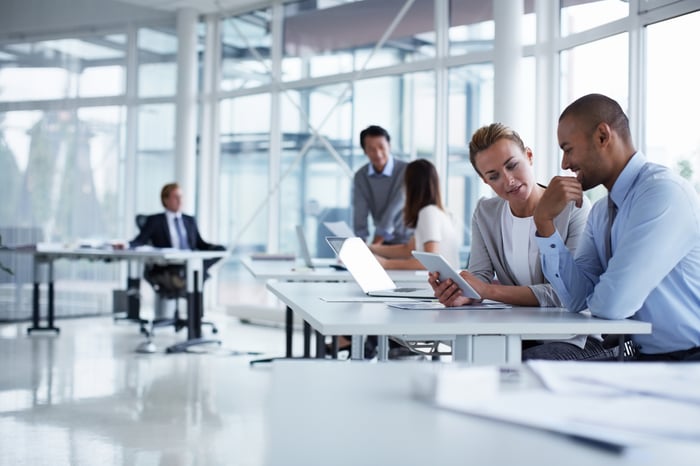 Colleagues in a steel and glass-walled office having a discussion while looking at a tablet