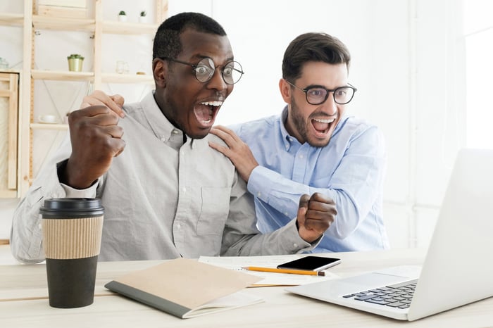 Two persons celebrating as they watch a computer screen.