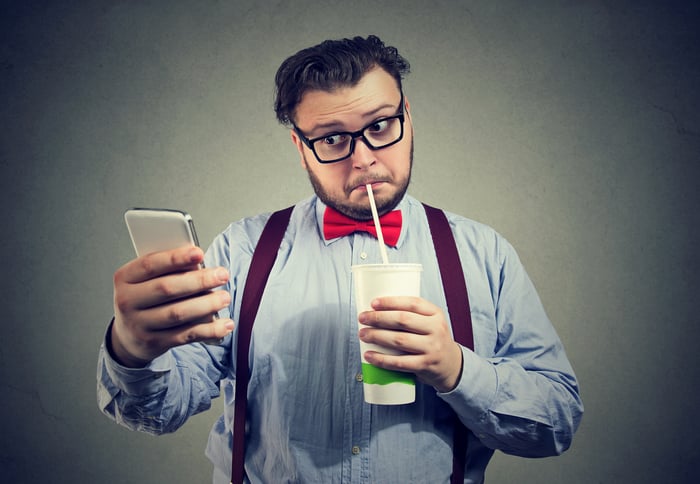 Someone is sipping a drink and looking skeptically at their phone.