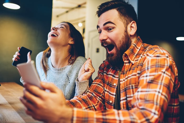 Two people cheering while looking at their phones.