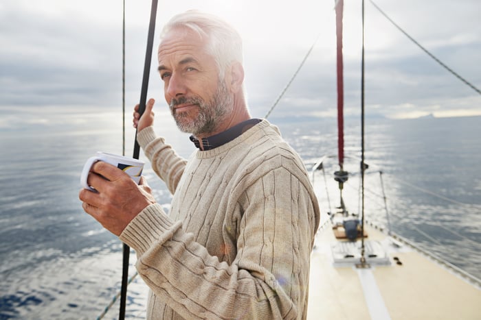 Senior person on sailboat holding mug.