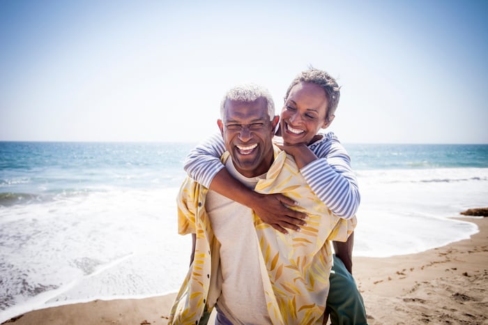 Couple on beach going for piggyback ride and smiling.