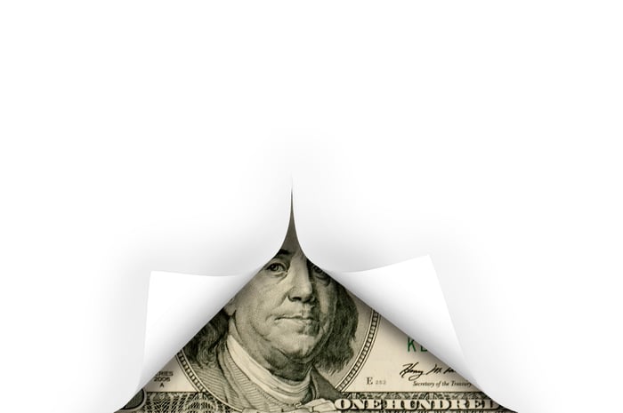 A hundred dollar bill unveiled beneath a white cover. 