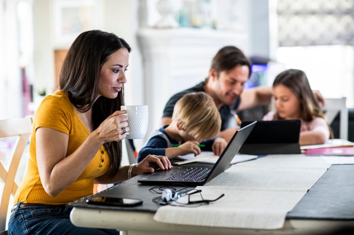 Woman holding a mug while using her laptop at a table with her family.