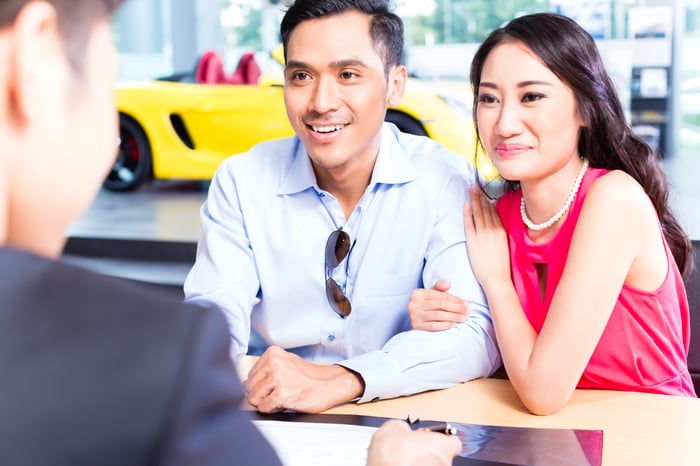 Two smiling people signing contracts for a purchase at a car dealership.