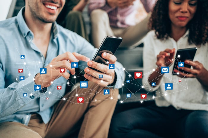 Two people using their smartphones, with a digital network of emoticons overlaid.