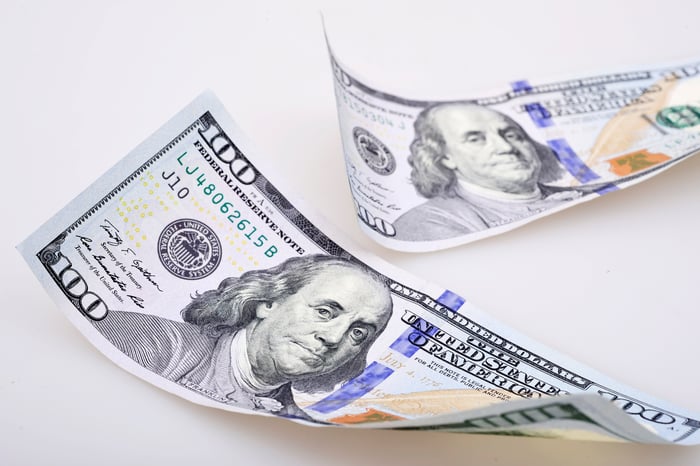 Two slightly curled one hundred dollar bills placed on a counter.