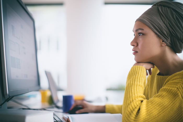 Person sitting at a desk looks at content on a large monitor.